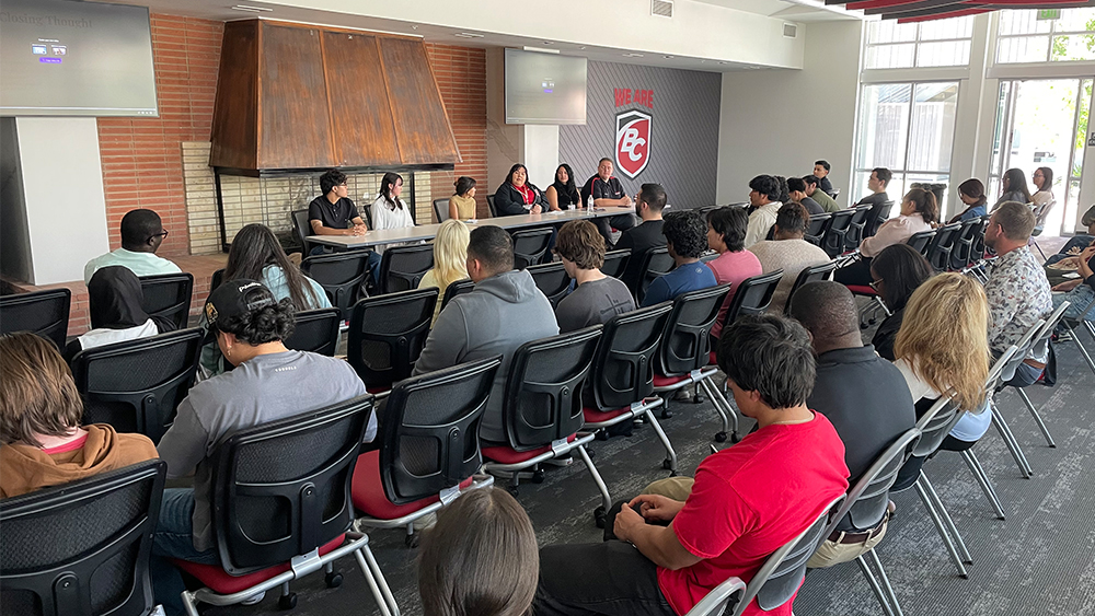 student panelists sitting at a table facing a medium sized audience; BC logo in the back
