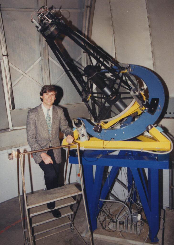 a man in suit standing next to a telescope