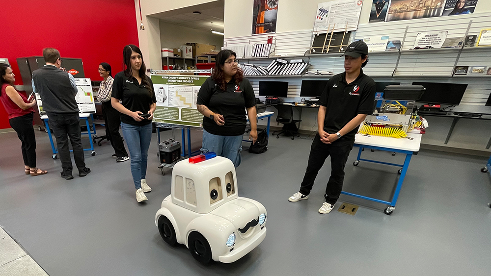 three students wearing black shirts observing a remote controlled miniature police car
