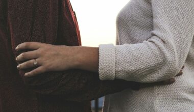 Close-up of two people embracing; one wears a round diamond solitaire ring on their left ring finger. One wears a dark burgundy dotted top, the other a light gray knit sweater.