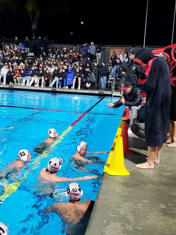 La Jolla High coach Tom Atwell (crouching) speaks to his boys water polo team during the CIF San Diego Section Open Division championship game in 2025. (Ashley Mackin-Solomon)