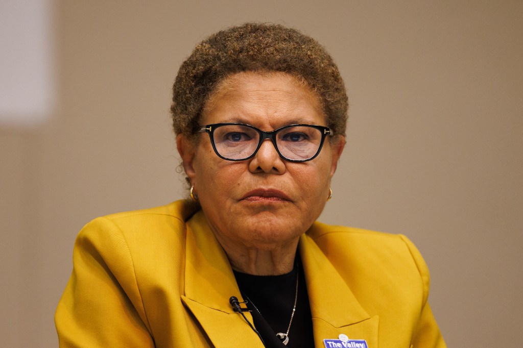 Los Angeles Mayor Karen Bass in a yellow blazer, glasses, and a lavalier microphone, at a debate.