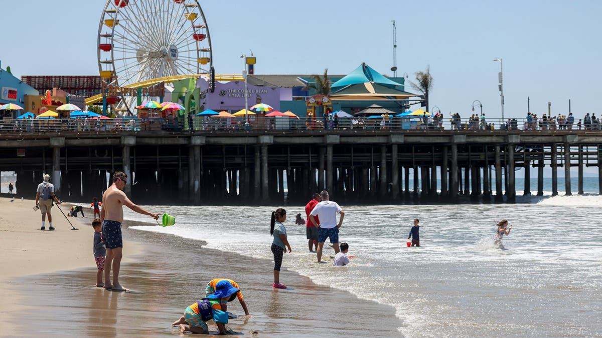 People play on the beach of Santa Monica Pier with the ferris wheel in the background.