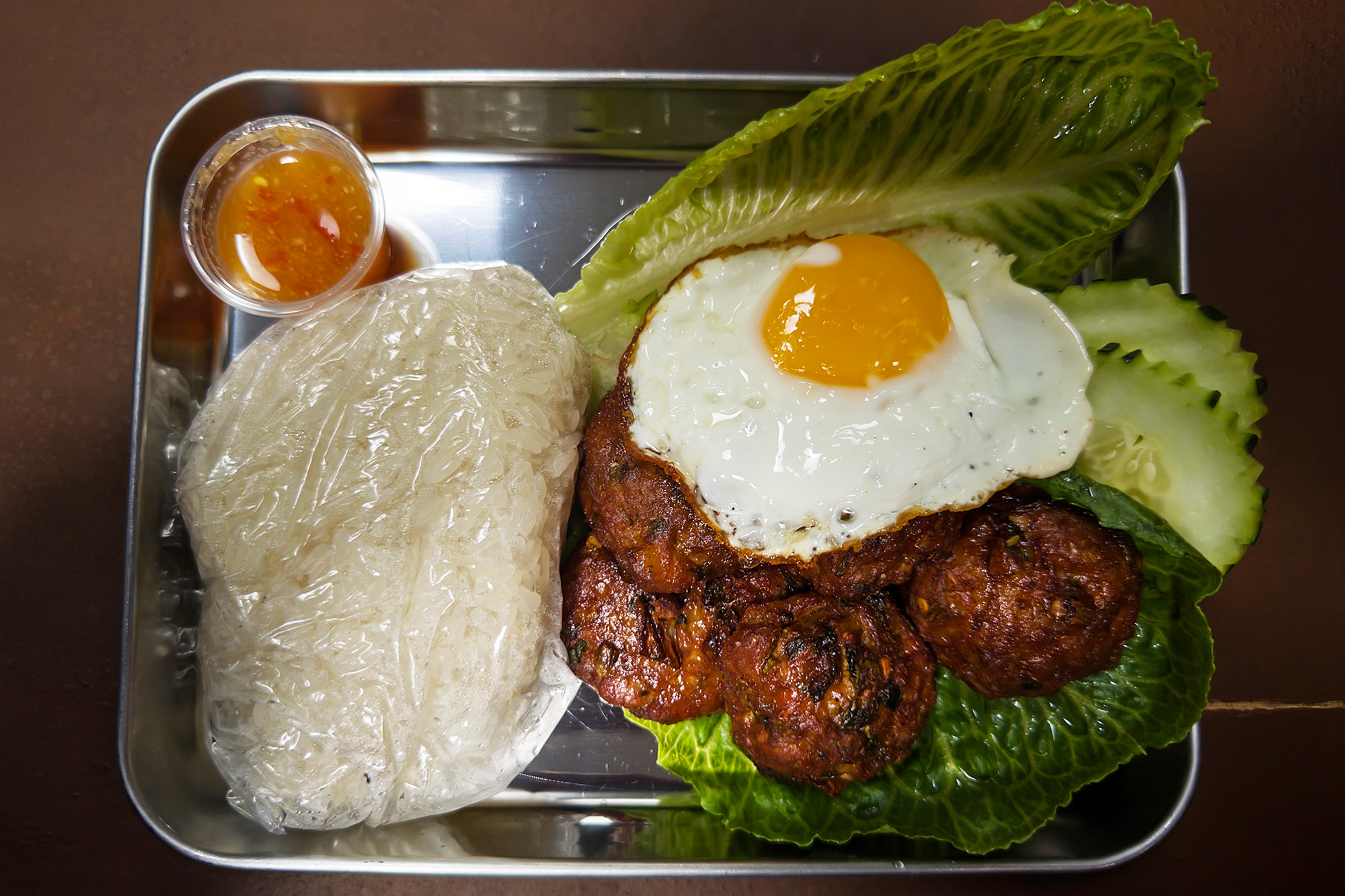 Sticky rice, sausage balls and fried egg on a metal tray.
