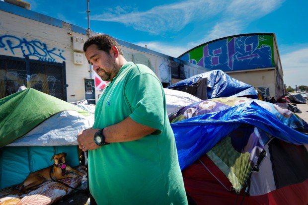 Manolo Di Pradonelli, 57, watched from his encampment on a private lot along National Avenue as a city crew collected trash and debris from nearby sidewalks during a sweep. (Nelvin C. Cepeda / The San Diego Union-Tribune)