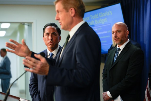On April 15, Mayor Todd Gloria and Rolando Charvel, the city's chief financial officer, watched as Michael Zucchet addressed news reporters at City Hall.   (Nelvin C. Cepeda / The San Diego Union-Tribune)