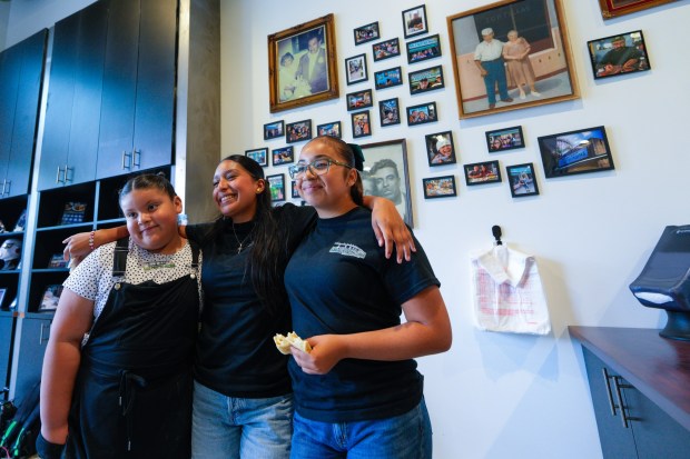 On Tuesday, May 12, 2026, in San Diego, CA, just before the reopening of Las Cuatros Milpas in Barrio Logan, family members Casey Calderon (l), Valery Estudillo (m), and Leah Estudillo (r) posed for a photo next to the wall displaying their family photos. (Nelvin C. Cepeda / The San Diego Union-Tribune)