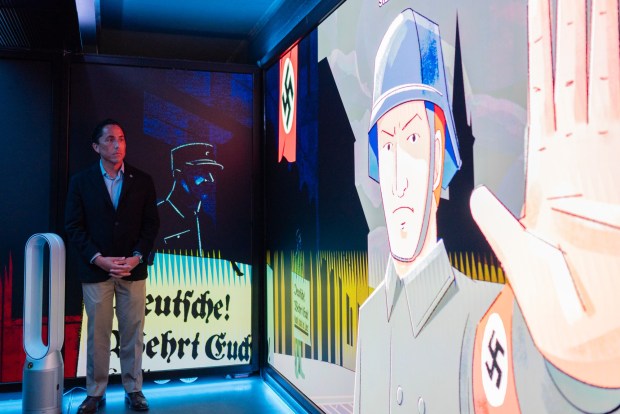San Diego Mayor Todd Gloria watches "Holocaust 101," an interactive video shown inside the Spark Interactive bus before speaking at its launch event at Crownair Aviation on May 3, 2026. (McKenzie Patterson / For The San Diego Union-Tribune)