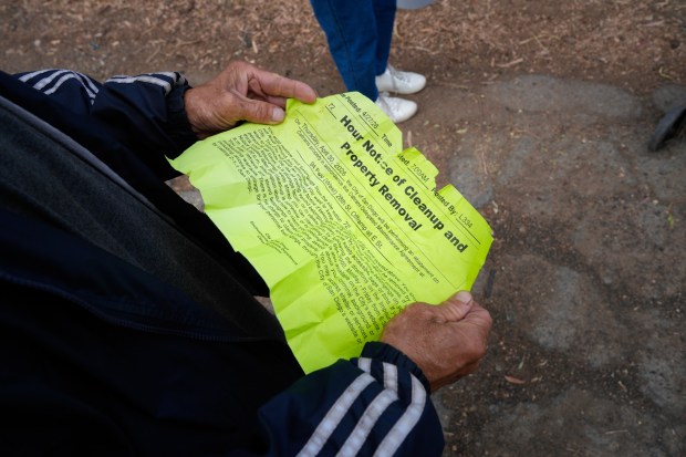Jason Borja pulls out the notice of an encampment sweep that the city posted where he camps near the state Route 94 westbound freeway. (Nelvin C. Cepeda / The San Diego Union-Tribune)