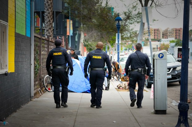 Near the corner of 16th and J Street downtown, Sgt. Christopher Smith (right) and his team walk up to an encampment to inform people of a scheduled abatement. (Nelvin C. Cepeda / The San Diego Union-Tribune)