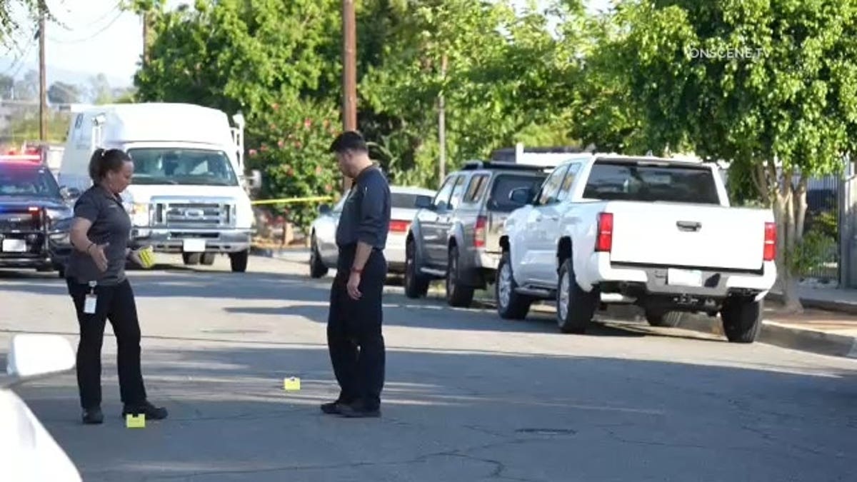 One investigator gestures to another near evidence markers in the street