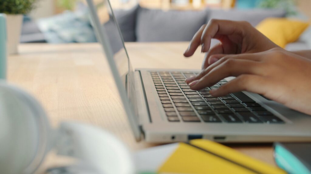 A side view of a person's hands typing on a silver laptop.