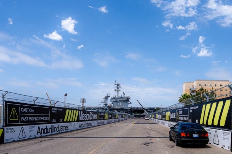 A large ship, with the number 70 on display, can be seen behind a track with a banner on the side that reads "caution: fast-moving vehicles."