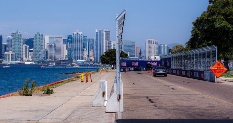 A city skyline can be seen across the water from where walls are going up along a curved stretch of road.