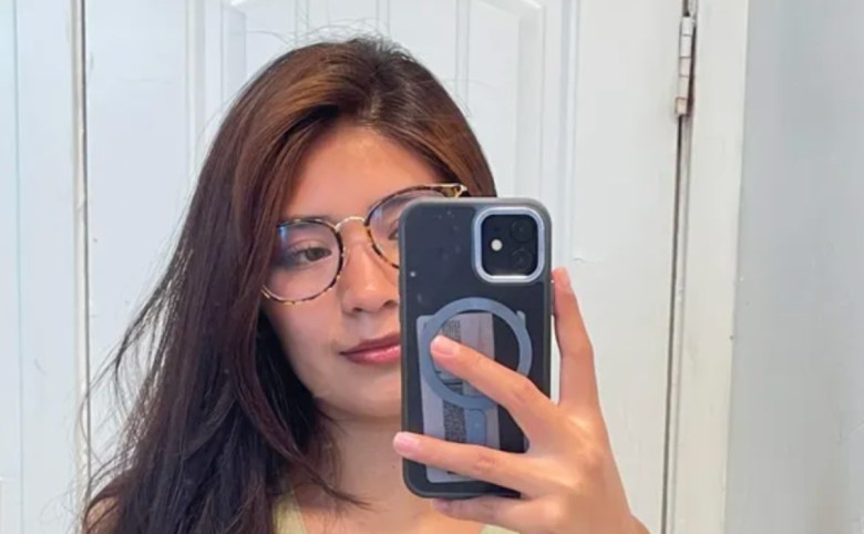 A long-haired woman looks at her camera pointed toward a mirror while taking a selfie.