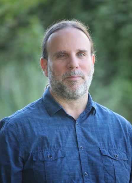 A man in a button-down shirt poses for a portrait outdoors.