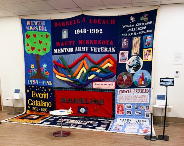 Panels of a quilt that display the names of several people hanging from a wall.