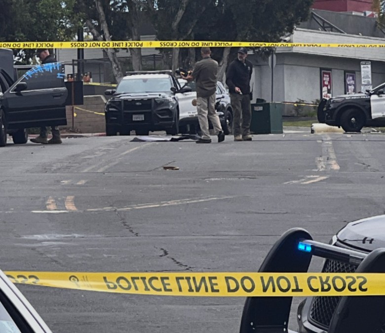 crime scene tape marks marks an area in which police stand guard, with some examining a black sedan with several pieces of tape affixed to the driver's side window.