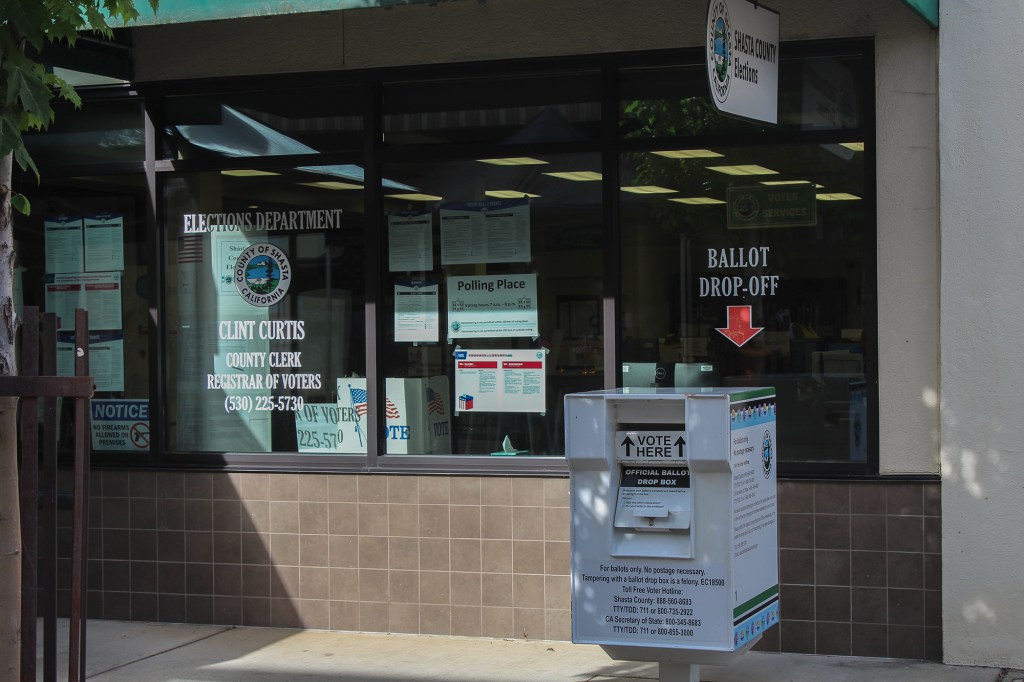 The outside of a building for a local election office, where a white mail-in drop box can be seen nearby.