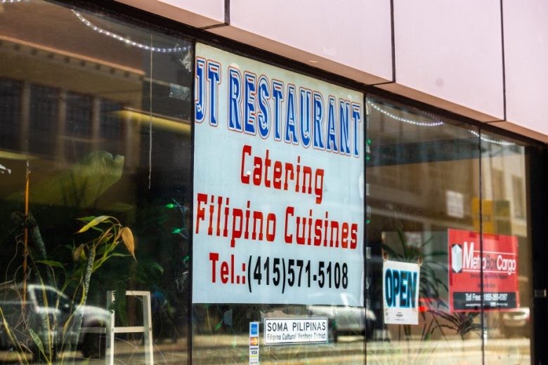 A restaurant window displays a sign advertising catering for Filipino cuisines with a phone number and an "OPEN" sign.