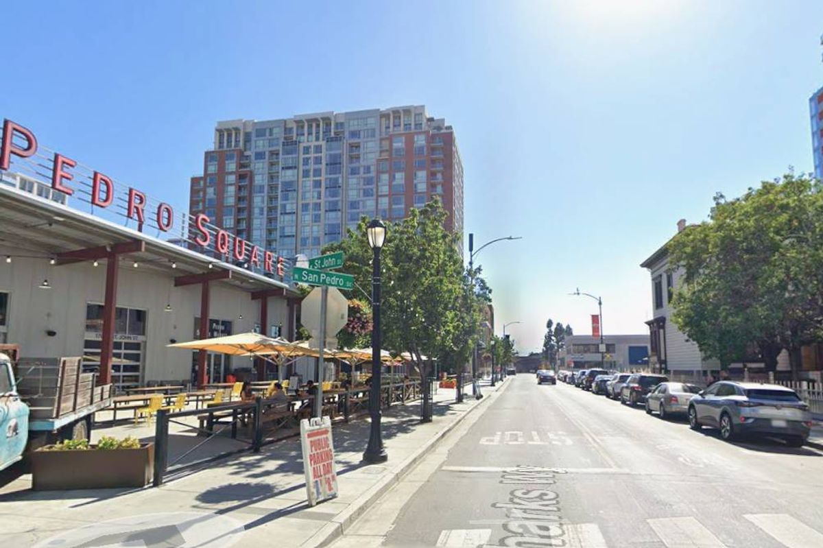 An image showcasing an urban street with a prominent building in the background. The building is prominently displayed with red lettering reading "PEDRO," indicating a likely commercial or retail establishment. The street is lined with streetlights, trees, and parked cars on the side, with a clear view of the sky overhead. The setting appears to be a typical city street, with an empty road and buildings lining either side.