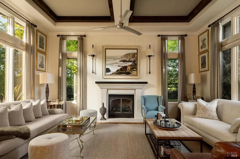 Bright formal living room featuring dual neutral sofas, large windows, and a central fireplace