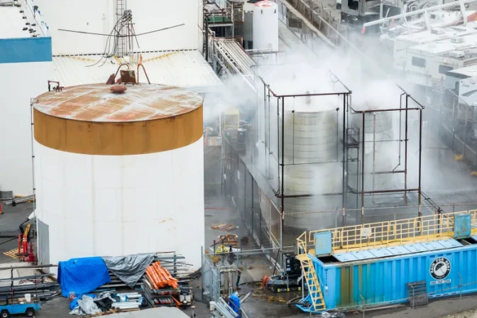 A slightly high angle view of a large tank next to smaller tanks outside, which have steam coming out of them.