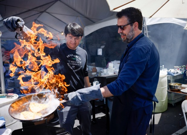 Ari Delopoulos, right, prepares saganaki with the help of Adam Bell, left, at the Meze & Cheese Bar the San Jose Greek Festival at St. Nicholas Greek Orthodox Church in San Jose, Calif., on Sunday, May 31, 2026. (Nhat V. Meyer/Bay Area News Group)