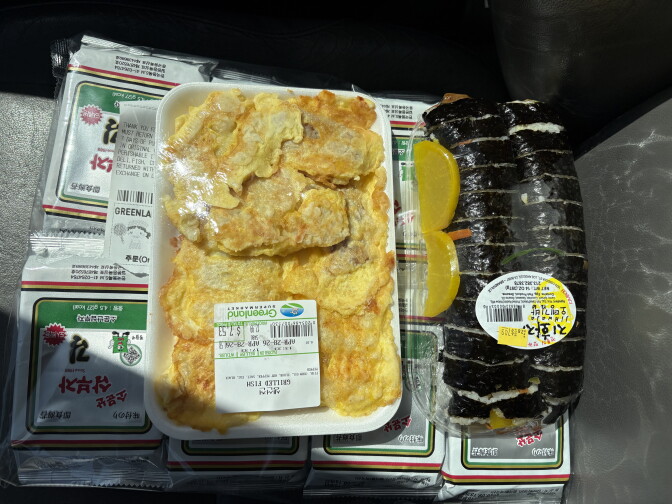 A wrapped packet of dumplings sits next to a seaweed wrapped dish, on top of packets of seaweed.