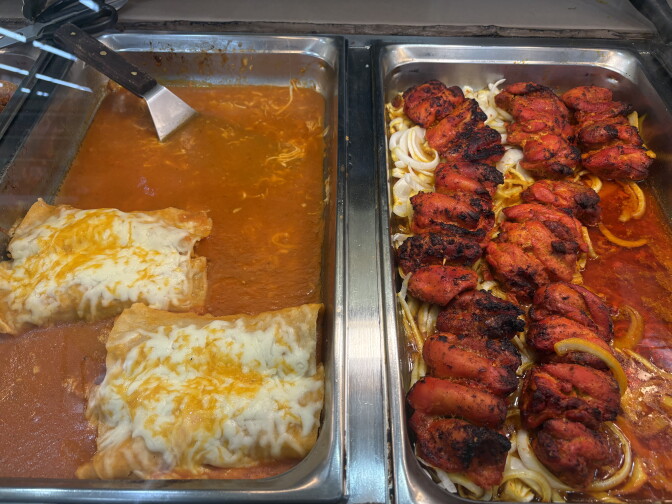 Two metal dishes contain Mexican enchiladas covered with cheese on the left, and red savory chicken wings in an onion sauce on the right.
