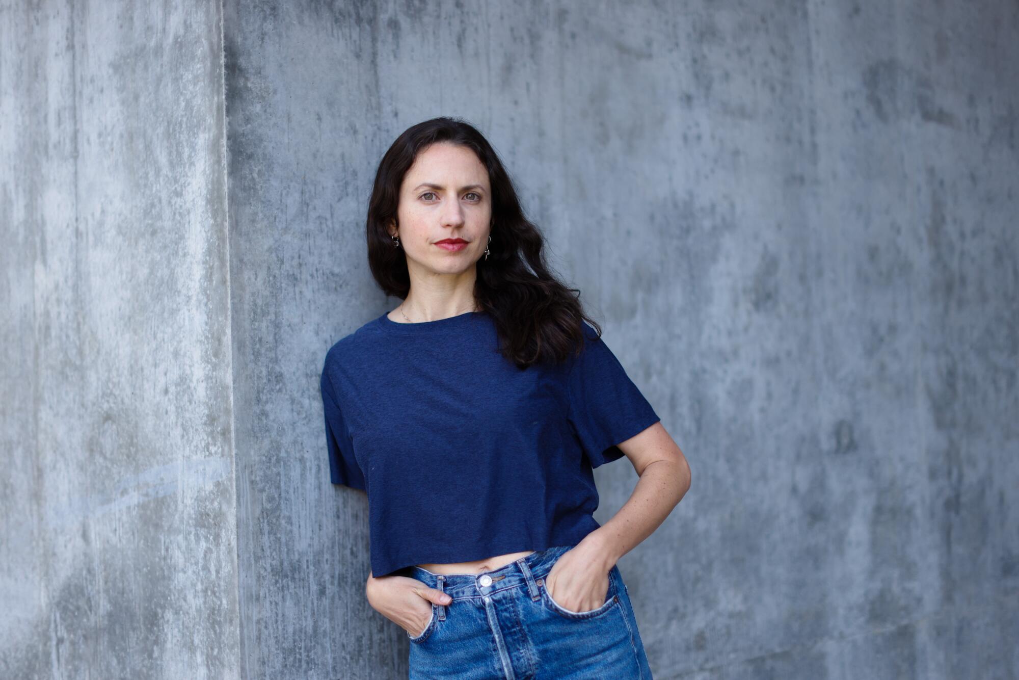 A woman poses against a concrete backdrop.