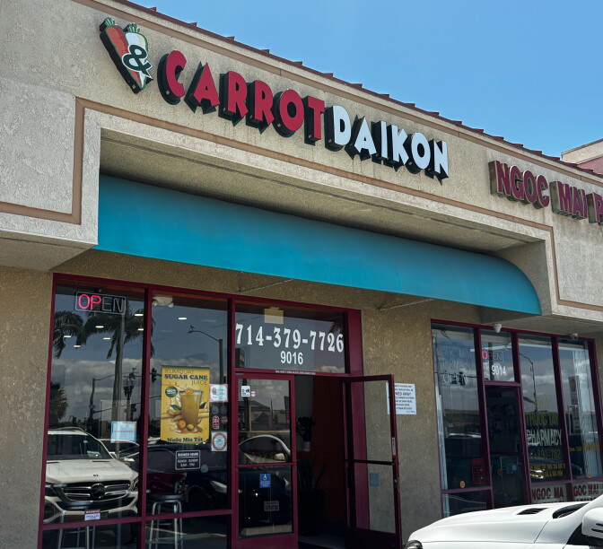 The exterior of Carrot & Daikon Banh Mi on Bolsa Avenue in Westminster, with a teal awning and red door frame.