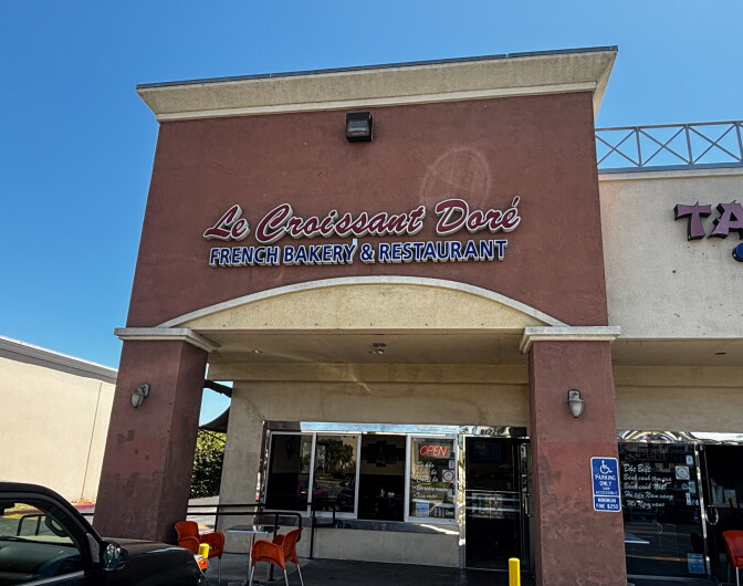 The exterior of Le Croissant Doré French Bakery & Restaurant on Bolsa Avenue in Westminster, with the restaurant's name in cursive lettering against a reddish-brown facade.