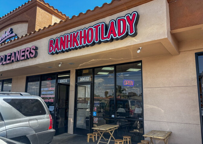 The exterior of Bánh Khọt Lady on McFadden Avenue in Westminster, with a bold red and white sign and small bamboo tables and stools outside the entrance.
