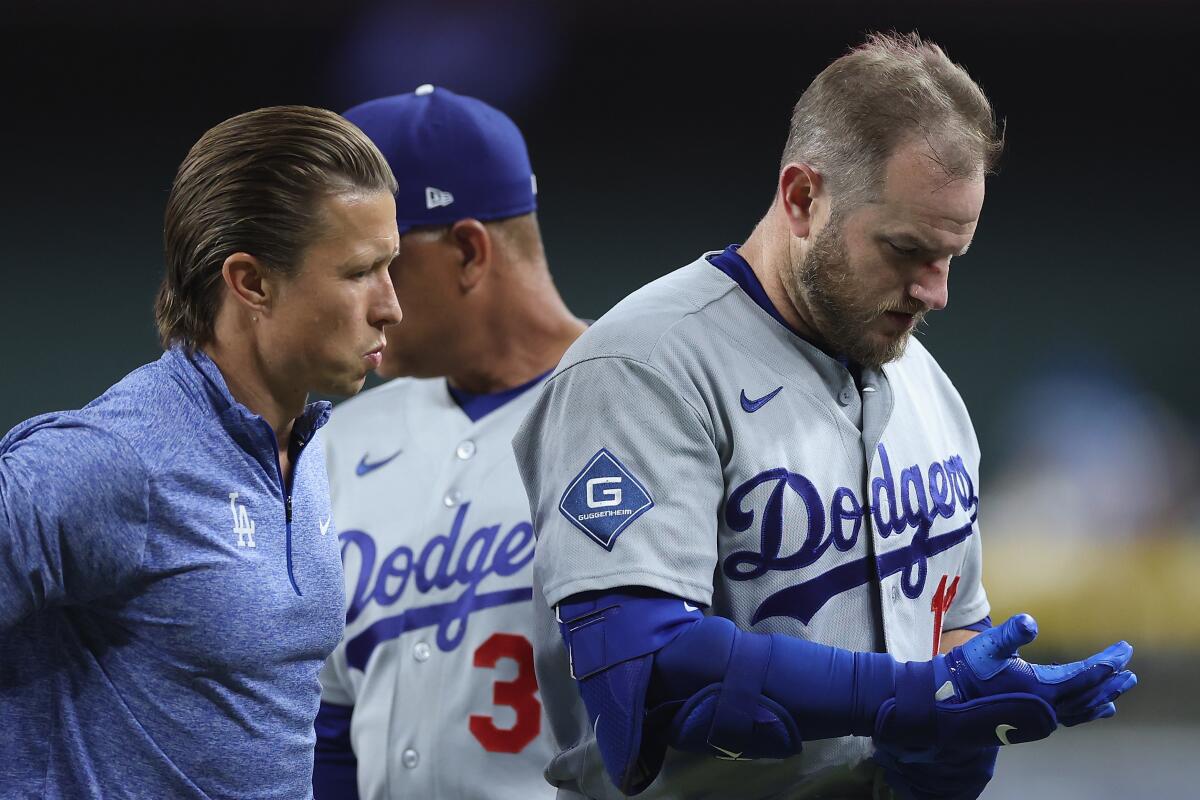 Dodgers baserunner Max Muncy walks off the field with a team trainer after colliding with Arizona's Ildemaro Vargas.