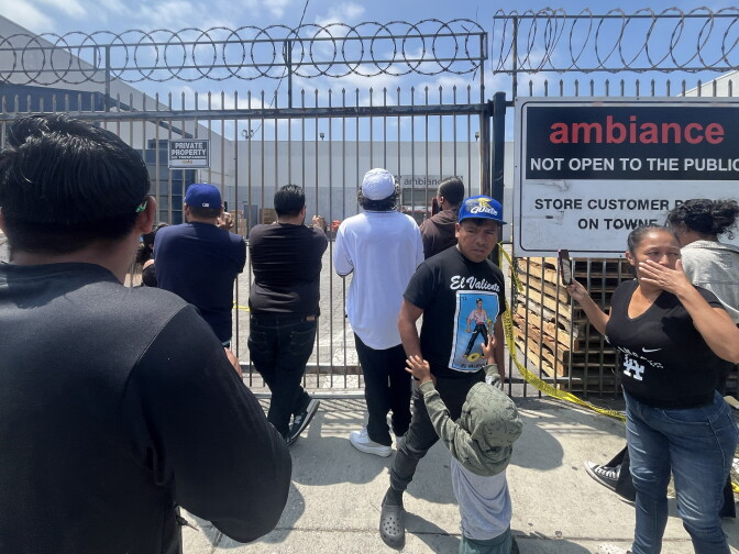 About 9 people, including one child, stand in front of a gate with barbed wire. Some are turned toward the gate. A sign on the gate reads: "Ambiance. Not open to the public."