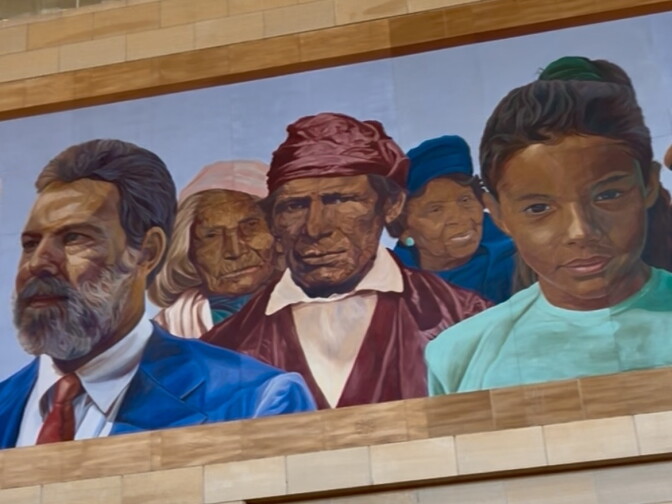 A mural shows several people of various ages and ethnicities, wearing blue, brown and teal clothes.