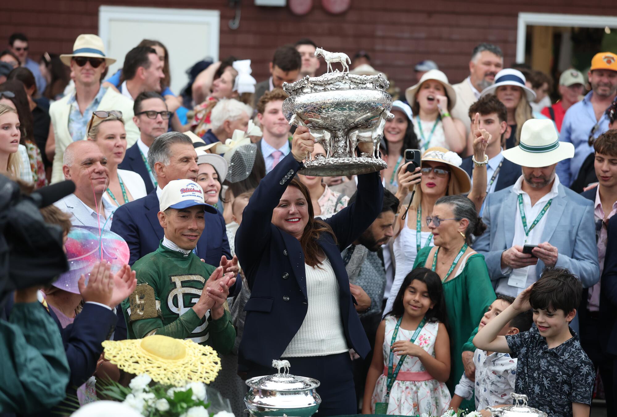 Trainer Cherie DeVaux lifts the August Belmont Trophy as she stands next to winning jockey Jose Ortiz.