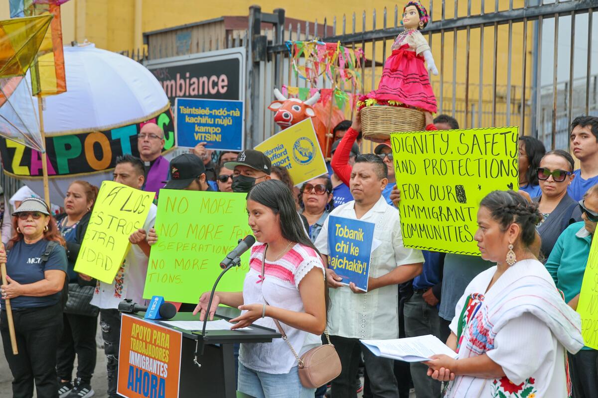 A young woman speaks at a news conference with people holding protest signs.
