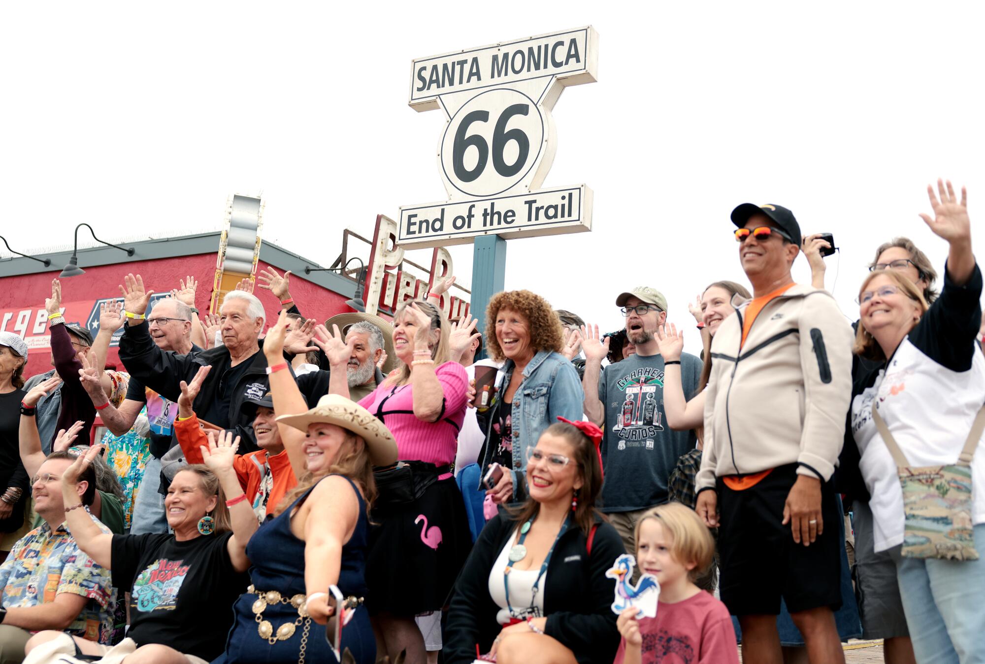People pose for a photo in front of a sign that says Santa Monica 66 End of the Trail