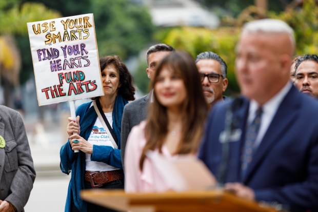 Jess Baron, executive director of Guitars and Ukes in the Classroom, holds a sign during a press conference on arts and culture funding outside City Hall on Friday, June 5, 2026. (Kristian Carreon / The San Diego Union-Tribune)