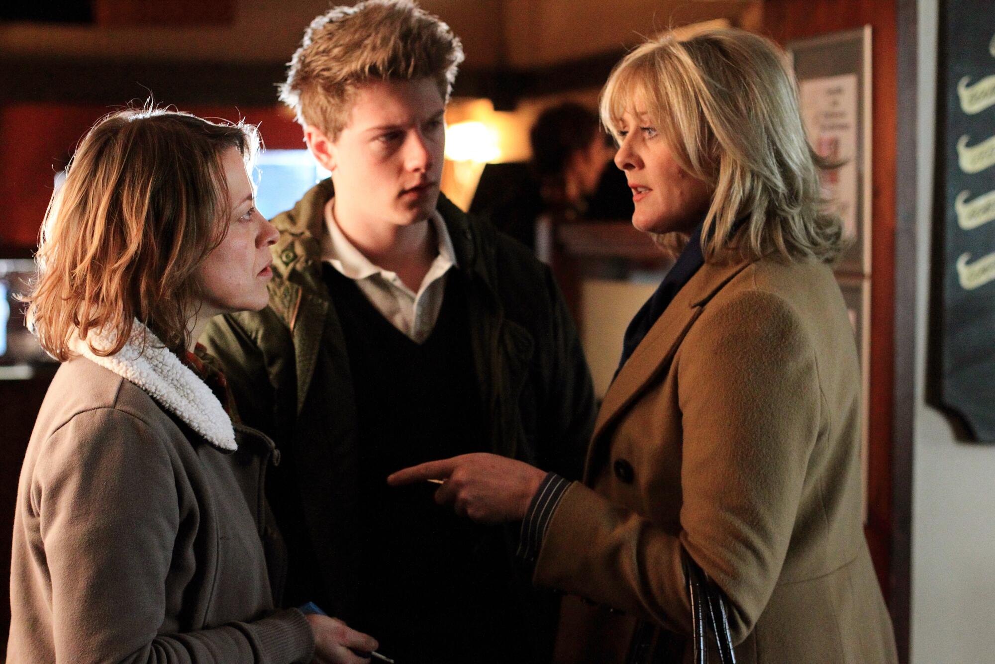 Three people standing around each other with stern looks on their faces.