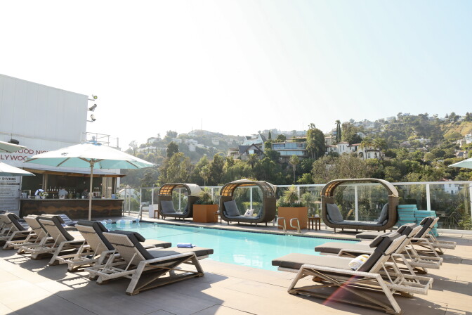 Gray and white beach chairs surround a pool. At the end of the pool is a bar.