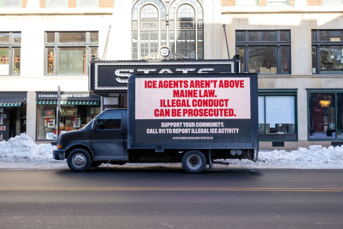 A truck with a billboard is parked on a snowy street.