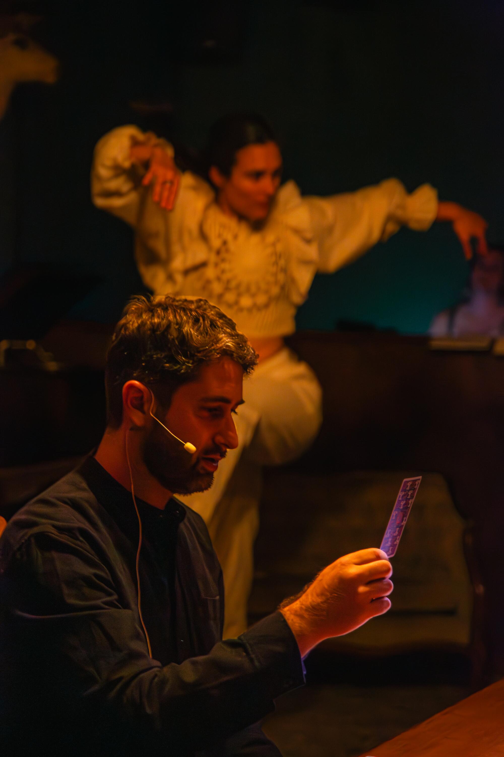 A man holding a tarot card with a dancer behind him. 