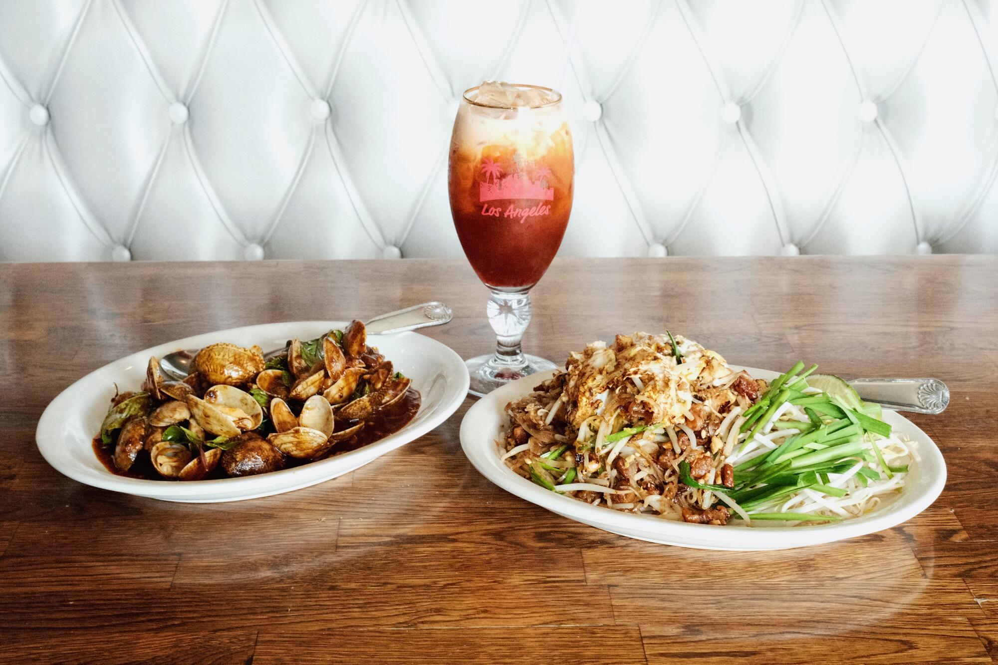 Sautéed clams with Thai basil and chili sauce, left, with pad Thai Sukhothai and Thai iced tea on a wood table