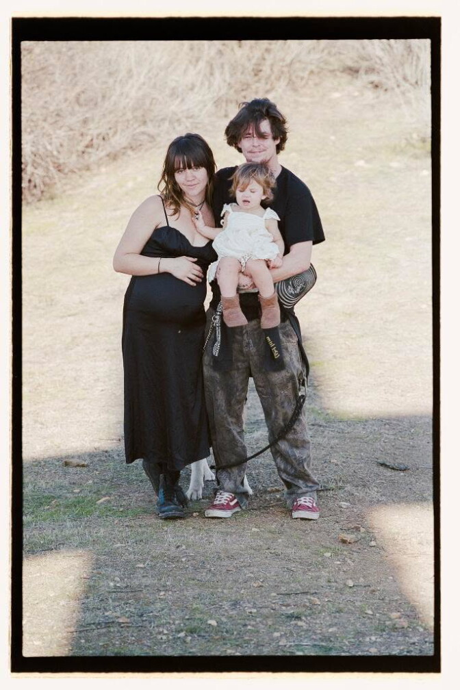 A pregnant woman stands next to a man holding a young girl.