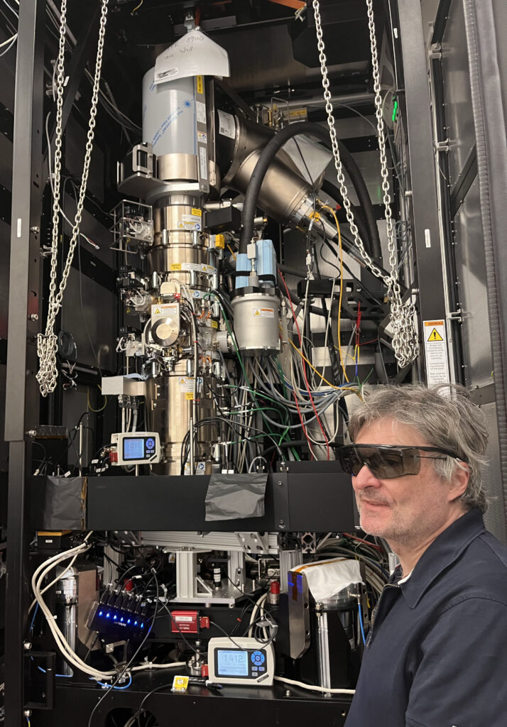a man in dark glasses standing in front of a tall complex apparatus