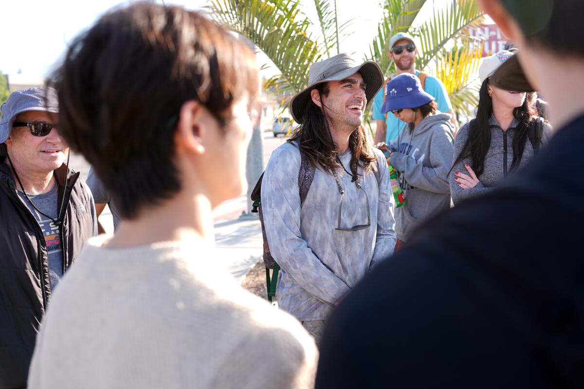 A man in a hat and long sleeves talks to a group of people circled around him.