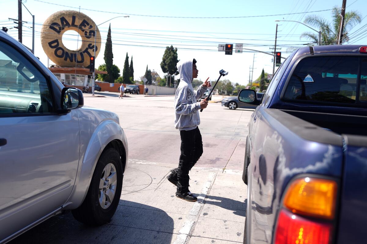 A teen in a hoodie holds a squeegee as cars pass by.